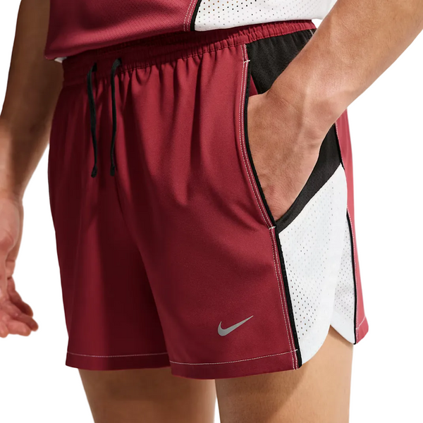 En person i rødbrune Nike Retro 4" Brief-Lined Running Shorts (Herre, Team Crimson/Black/Reflective Silv) med sorte og hvide mesh-sidepaneler har sin højre hånd i lommen. Nike-logoet vises nær venstre kant for et stilfuldt look.