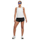 En person står med ansigtet fremad, det ene ben let bøjet, iført en hvid Nike Dri-Fit Race Tank til kvinder, sorte shorts, hvide sneakers og blå reflekterende solbriller.