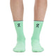 En person iført ON Elite Run Sock High Hyper-strømper i farven Celeste/Verdite, med et sort ON-logo og et tyndt gråt bånd øverst, står på en hvid baggrund. Disse unisex tekniske løbestrømper, der er designet til løbetræning, viser kun underbenene og fødderne på billedet.