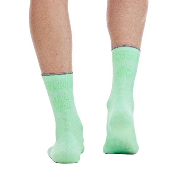 En persons underben og fødder ses bagfra, iført On Elite Run Sock High Hyper i unisex-farvekombinationen Celeste/Verdite. Disse tekniske løbestrømper har synlige strikmønstre ved hælen og anklen og er designet til optimal løbetræning. Baggrunden er ensfarvet hvid.