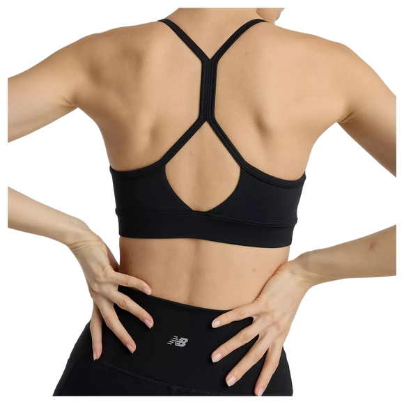 En kvinde ses bagfra iført New Balance Essential Yoga Bra, Dame, Black og sorte leggings med New Balance-logo. Hendes hænder hviler på lænden, og tøjet er lavet af blødt, åndbart materiale.