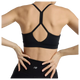 En kvinde ses bagfra iført New Balance Essential Yoga Bra, Dame, Black og sorte leggings med New Balance-logo. Hendes hænder hviler på lænden, og tøjet er lavet af blødt, åndbart materiale.