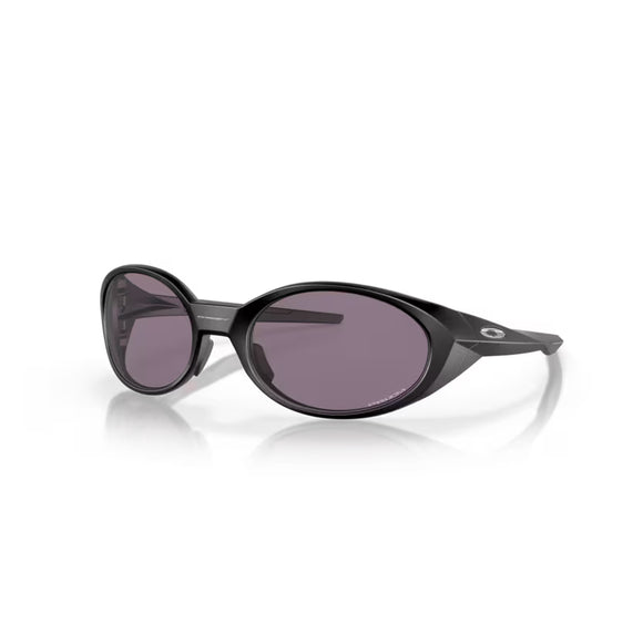 Et par Oakley Eye Jacket Redux solbriller i mat sort, med Prizm Grey linser og glatte ovale stel med en subtil metallisk detalje nær tindingen, vist på en hvid baggrund.