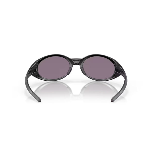 Et par Oakley Eye Jacket Redux-solbriller i Matte Black med Prizm Grey-glas er vist forfra på en hvid baggrund, med armene let åbne og en refleksion synlig nedenunder.