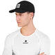En person, der bærer en Saysky Flow-kasket (unisex, sort) og en hvid, struktureret langærmet trøje i åndbart, hurtigtørrende stof med Saysky-mærket og stjernelogoet på både kasketten og trøjen, kigger til venstre foran en ensfarvet hvid baggrund.