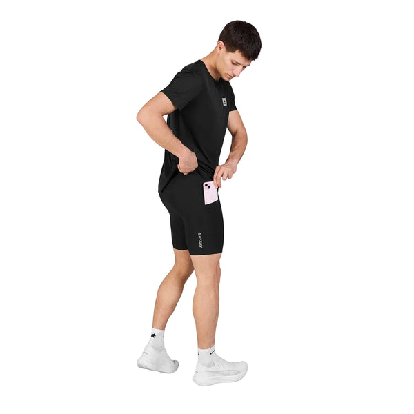 En mand iført sorte Saysky Flow+ Race Short Tights 7″, Herre, Black og en sort T-shirt tager en smartphone frem fra en lomme på siden af sine shorts.