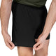 En person iført et par Saysky Flow Shorts 5′’ til mænd i sort og en grøn skjorte står og holder fast i shortsens nederste kant med begge hænder for at vise stoffet frem. Personens arme og en del af lårene er synlige.