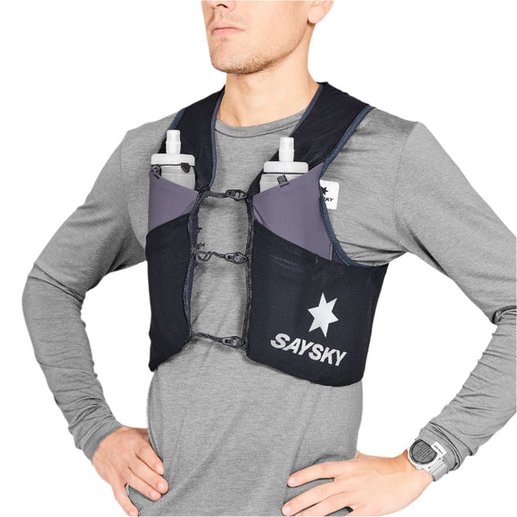 Iført en grå langærmet skjorte og Saysky Flow Vest 101 8L, Unisex, Black - med bløde flasker i forlommerne, SAYSKY-branding, stjerneemblem og 8L-opbevaring - står en person med hænderne på hofterne.