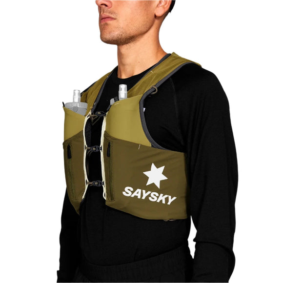 En person er iført en sort langærmet skjorte og en grøn Saysky Flow Vest 201 12L med et hvidt stjernelogo. To bløde flasker er synlige i forlommerne og viser, at denne unisex-vest er ideel til at holde sig hydreret på løbeturen.