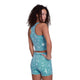 En person med krøllet hår står sidelæns og kigger sig over skulderen. De er iført Saysky Flower Combat Crop Top, Dame, Light Blue Flower - medium støtte og ideel til løbere - med et let abstrakt mønster på hvid.