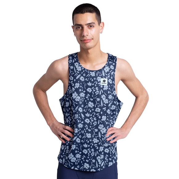 En person står med hænderne på hofterne iført Saysky Flower Combat Singlet, Herre, Blue Flower - en marineblå løbetop med et lyseblåt blomstermønster - og mørke shorts på en almindelig hvid baggrund.