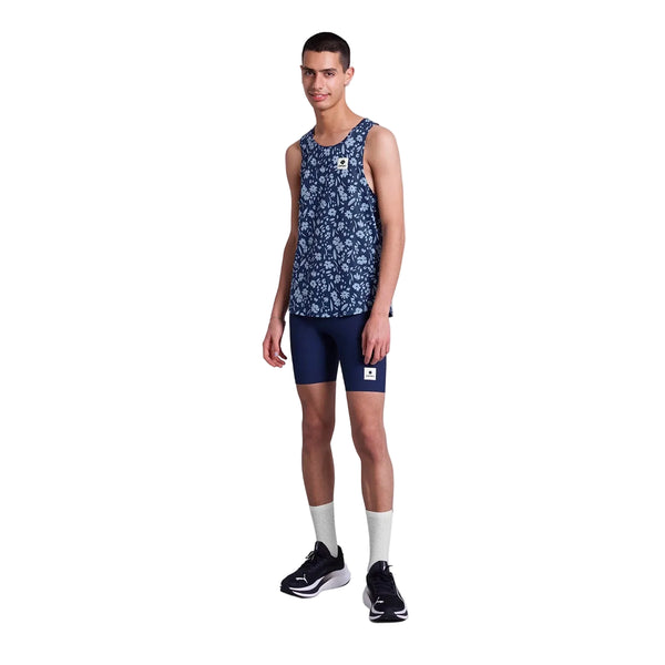 En person ser frem for sig iført Saysky Flower Combat Singlet, Herre, Blue Flower, marineblå shorts, hvide strømper og sorte sportssko mod en almindelig hvid baggrund.
