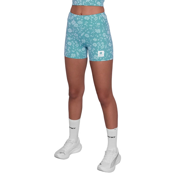 En person er iført en matchende lyseblå crop top og Saysky Flower Combat+ Short Tights 4" (Dame, Light Blue Flower) med et hvidt blomsterdesign, sammen med hvide sportssokker og sneakers. Personens hoved er ikke synligt på billedet.