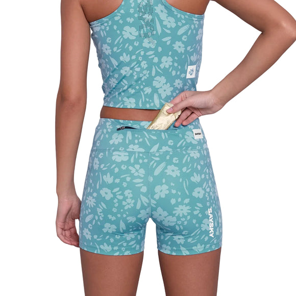 En person iført Saysky Flower Combat+ Short Tights 4" Dame i Light Blue Flower lægger en lille ting i baglommen med lynlås, hvilket fremhæver blomstermønsteret og det funktionelle design set bagfra fra taljehøjde.