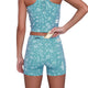 En person iført Saysky Flower Combat+ Short Tights 4" Dame i Light Blue Flower lægger en lille ting i baglommen med lynlås, hvilket fremhæver blomstermønsteret og det funktionelle design set bagfra fra taljehøjde.