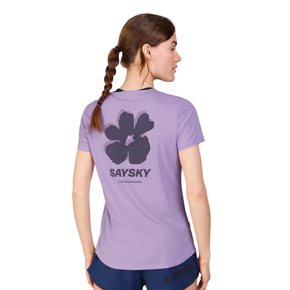 En kvinde med flettet hestehale bærer Saysky Flower Flow T-Shirt, Dame, Purple, med en stor sort blomstergrafik og SAYSKY COPENHAGEN-tekst på ryggen, sammen med marineblå shorts.
