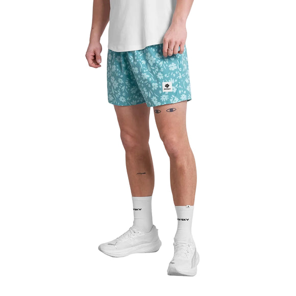 En person iført hvid t-shirt, Saysky Flower Pace Shorts 5" Herre Light Blue Flower, hvide strømper og hvide sneakers står på en almindelig baggrund.