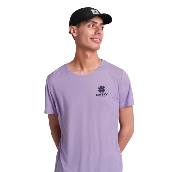 En mand iført Saysky Flower Flow T-shirt, Herre, Purple - med blomstergrafik og logo - står på en hvid baggrund, smiler og kigger til siden.