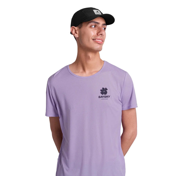 En mand iført Saysky Flower Flow T-shirt, Herre, Purple - med blomstergrafik og logo - står på en hvid baggrund, smiler og kigger til siden.