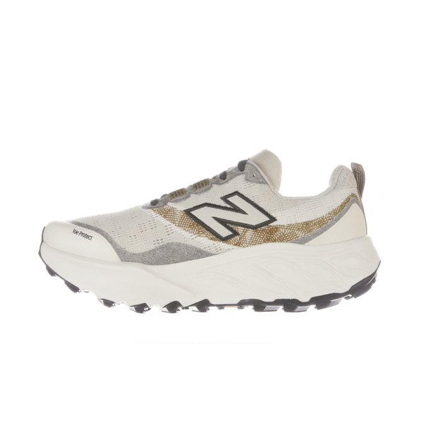 New Balance Freshfoam Hierro V9, Dame, Angora er en hvid og grå trailløbesko med en tyk sål, sort N-logo, guldfarvede detaljer og sort slidbane. Den vises på en almindelig hvid baggrund.
