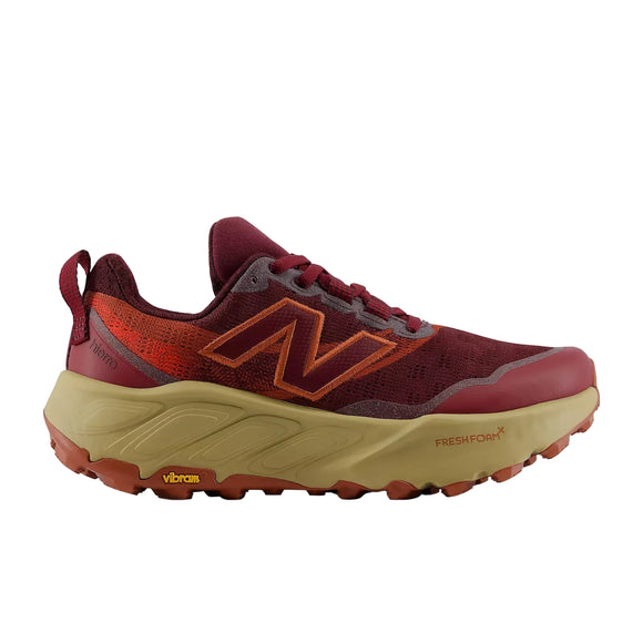 En New Balance Freshfoam Hierro V9 Dame trailsko i farvekombinationen »Mulled Wine«, der er holdt i rødbrune og orange nuancer, med en tyk, lysebrun og orange Vibram-sål, en åndbar overdel i mesh samt Fresh Foam X-støddæmpningslogoet på siden, vises i et profilbillede fra venstre side på en hvid baggrund.