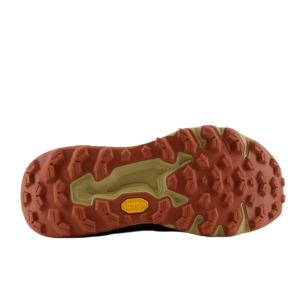 Billedet viser sålens mønster på en sko med en robust, orange-brun gummisål og et gult Vibram-logo i midten. Mønsteret består af adskillige kantede knopper, der sikrer godt greb, hvilket er karakteristisk for New Balance Freshfoam Hierro V9 til kvinder i farvevarianten »Mulled Wine«.