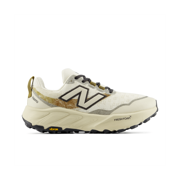 New Balance Freshfoam Hierro V9, Herre, Angora har et hvidt og beige design med sorte og guldfarvede detaljer, et sort N-logo, en Vibram-sål og Fresh Foam X-støddæmpning. Vist i sideprofil på hvid baggrund.