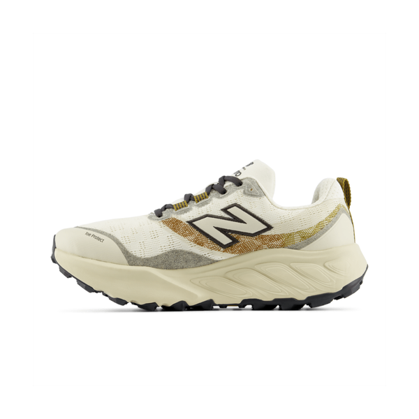 New Balance Freshfoam Hierro V9 Herre i farven Angora har et hvidt og beige design med et sort N-logo, guld- og grå detaljer, sorte snørebånd og en kraftig, off-white sål med sort mønster. Vist i sideprofil på en ensfarvet baggrund.