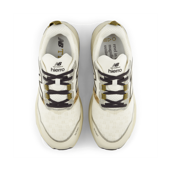 Et par New Balance Freshfoam Hierro V9 Herre Angora-sneakers i hvid og beige med sorte og guldfarvede detaljer, set ovenfra, har mærket på tungen og indersålerne.
