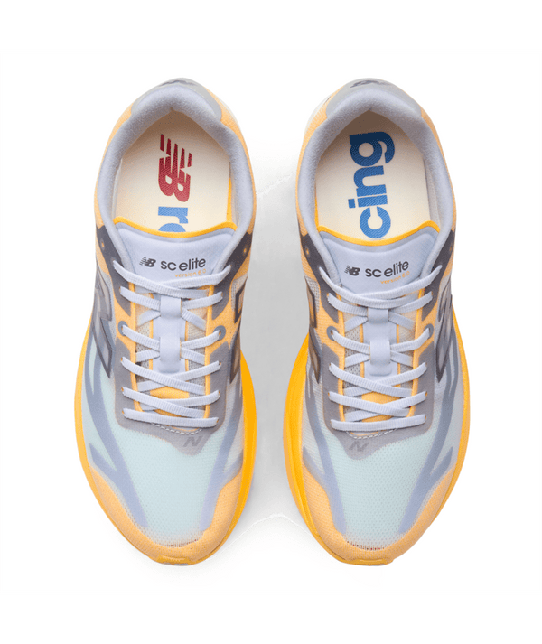 Oversigtsbillede af et par New Balance FuelCell Supercomp Elite V6, Herre, Satsuma Orange x NYC Marathon løbesko i lysegrå, gul og orange med hvide snørebånd. Den venstre indersål har et rødt logo, mens den højre indersål har blå tekst. Designet som konkurrencesko med carbonplade-konstruktion for optimal ydeevne. Mærkenavnet og modellen er trykt på tungen.