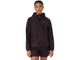 En person står med ansigtet vendt fremad iført en mørk, mønstret ASICS Fujitrail Packable-jakke til kvinder i farven Dark Aubergine, kombineret med matchende shorts. Outfitet har et diskret camouflage-inspireret design, der minder om en trail-løbejakke, og er forsynet med små ASICS-logoer på brystet og venstre ærme. Looket fremhæves på en ren, hvid baggrund.