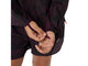 En person, hvor man kun kan se hænderne, en del af armen og lårene, justerer håndledsremmen på ærmet af en Asics Fujitrail Packable-jakke til kvinder i farven Dark Aubergine, som er kombineret med shorts, på en hvid baggrund.