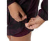 En person strammer nederkanten på Asics Fujitrail Packable Jacket, Dame, Dark Aubergine ved hjælp af en snor med stopper. Man kan kun se vedkommendes hænder og underkrop, og vedkommende har desuden et par matchende shorts på.