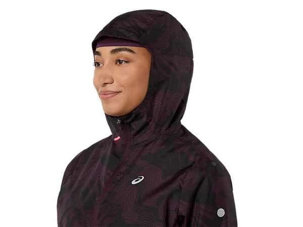 En person iført en mørk auberginefarvet ASICS Fujitrail Packable-jakke til kvinder med ASICS-logoet vender mod venstre og smiler let. Hætten er trukket op og dækker det meste af hovedet. Baggrunden er ensfarvet hvid.