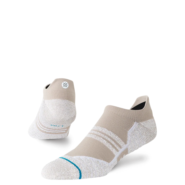 Et par Stance Fusion Grip Tab unisex-sokker i farvevarianten »Croissant«, der har et lavt, sporty design i beige og hvide nuancer, en struktureret sål med Fusion Grip Tab-teknologi, sidestriber, Stance FreshTek-fugtkontrol og et lille cirkulært logo på hælen – vist på en ensfarvet hvid baggrund.
