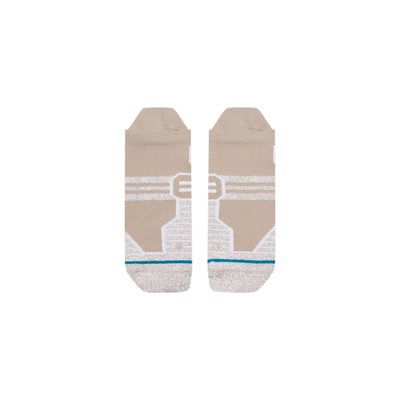 Stance Fusion Grip Tab-sokkerne i farvevarianten »Croissant« er et unisex-par beige ankelstrømper med hvide geometriske mønstre, grå tåspidser, en tynd blågrøn stribe tæt på tåområdet og markante, hvide, kantede designelementer i midten. Sokkerne er udstyret med Stances FreshTek-teknologi, der sikrer øget komfort og åndbarhed, og præsenteres her fladt på en ensfarvet hvid baggrund.
