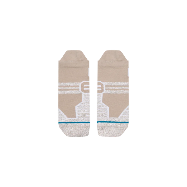 Stance Fusion Grip Tab-sokkerne i farvevarianten »Croissant« er et unisex-par beige ankelstrømper med hvide geometriske mønstre, grå tåspidser, en tynd blågrøn stribe tæt på tåområdet og markante, hvide, kantede designelementer i midten. Sokkerne er udstyret med Stances FreshTek-teknologi, der sikrer øget komfort og åndbarhed, og præsenteres her fladt på en ensfarvet hvid baggrund.