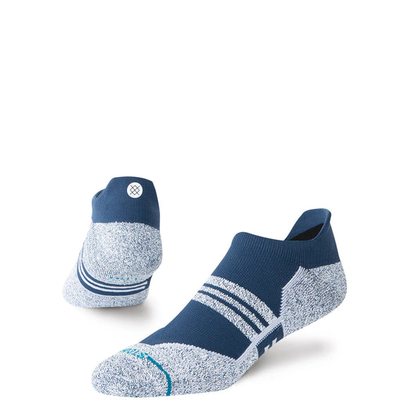Et par Stance Fusion Grip Tab unisex-sportsokker med lav skaft i marineblå med hvide striber, strukturerede tå- og hælområder samt et lille hvidt logo på bagsiden af den ene sok. Designet med skridsikre grippaneler for øget stabilitet, hvilket gør dem ideelle som løbestrømper. Vist på en ensfarvet hvid baggrund.