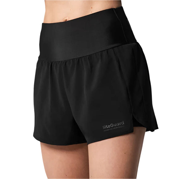 En person bærer Liiteguard Glu-Tech 2in1 Shorts, Dame, Black-højtaljede med en løs pasform og bred linning for løbetræning og hofte stabilitet. Liiteguard-logoet ses nederst til venstre på en hvid baggrund.