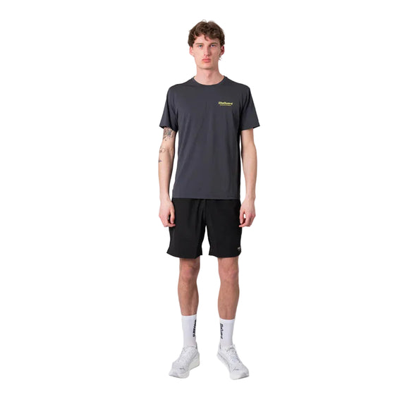 En mand står og kigger fremad iført en Liiteguard Ground-Tech T-shirt, Herre, Ebony/Neon Yellow - ideel til løbetræning takket være dens lugtbekæmpende egenskaber - sammen med sorte shorts, hvide sokker og hvide sportssko på en almindelig hvid baggrund.