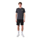 En mand står og kigger fremad iført en Liiteguard Ground-Tech T-shirt, Herre, Ebony/Neon Yellow - ideel til løbetræning takket være dens lugtbekæmpende egenskaber - sammen med sorte shorts, hvide sokker og hvide sportssko på en almindelig hvid baggrund.