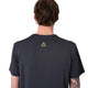 En person med kort brunt hår ses bagfra iført en Liiteguard Ground-Tech T-shirt, Herre, Ebony/Neon Yellow med lugtbekæmpende egenskaber og et lille gult symbol på ryggen. En del af en tatovering kan ses på venstre underarm.