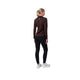 En person står med ryggen til i et simpelt studie iført Liiteguard Ground-Tech 1/4 Zip, Dame, Coffee Bean trøje, sorte leggings, hvide sokker og sneakers. Håret er sat op i en hestehale.