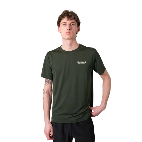 En person står på en hvid baggrund iført en Liiteguard Ground-Tech T-shirt, Herre, Army Green med sorte bukser. Den ene arm hviler på hoften og viser en underarmstatovering.