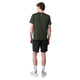 En person står med ryggen til kameraet iført en Liiteguard Ground-Tech T-shirt, Herre, Army Green, sammen med sorte shorts, hvide sokker og hvide sneakers på en almindelig hvid baggrund.