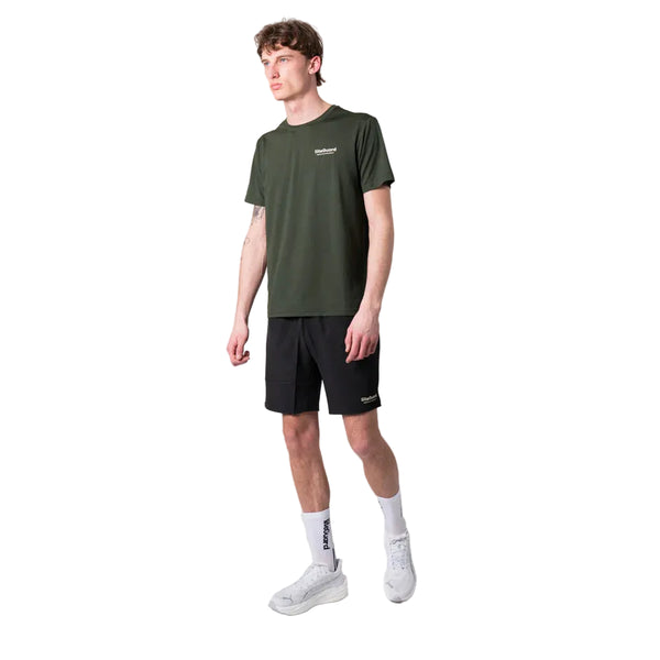 En mand står på en hvid baggrund iført en Liiteguard Ground-Tech T-shirt, Herre, Army Green, sorte shorts, hvide strømper og hvide sneakers. Han kigger til siden med venstre arm afslappet langs siden.