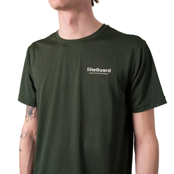 En person med lys hud og tatoveringer på venstre underarm bærer en Liiteguard Ground-Tech T-shirt, Herre, i Army Green med Liiteguard-logoet på venstre bryst.