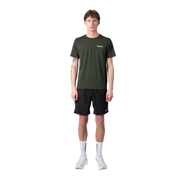 En person står med ansigtet fremad og er iført en Liiteguard Ground-Tech T-shirt, Herre, Army Green, sorte shorts, hvide strømper og hvide sportssko på en almindelig hvid baggrund.