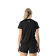 En kvinde med langt lyst hår i hestehale står med ansigtet vendt mod kameraet iført Liiteguard Ground-Tech T-shirt, Dame, Black - ideel til løbetræning - sammen med sorte shorts på en almindelig hvid baggrund.