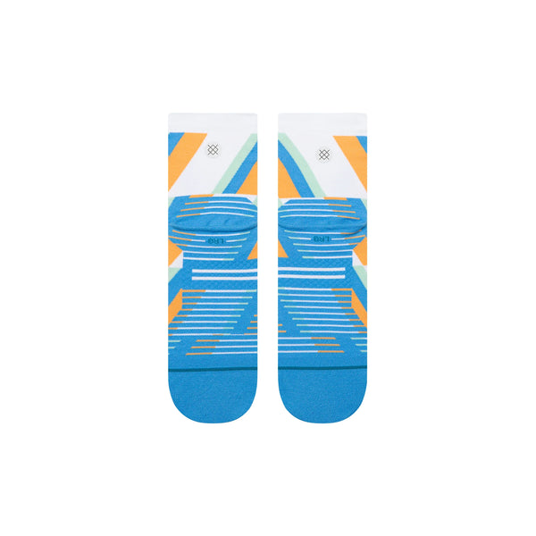 Et par Stance Gamma Ray UL Quarter unisex-strømper i blå med et geometrisk mønster i blå, orange, gul og hvid med ensfarvede blå tæer og hæle. Strømperne er vist liggende fladt side om side på en hvid baggrund.